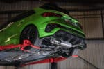 Scorpion RVS Sportuitlaat - Audi RS3 8Y Sportsback (OPF) - Met klep - Resonated uivoering met Carbon Fiber ovale uitlaatsierstukken vanuit de onderkant van de auto zichtbaar in gemonteerde toestand op een groene RS3